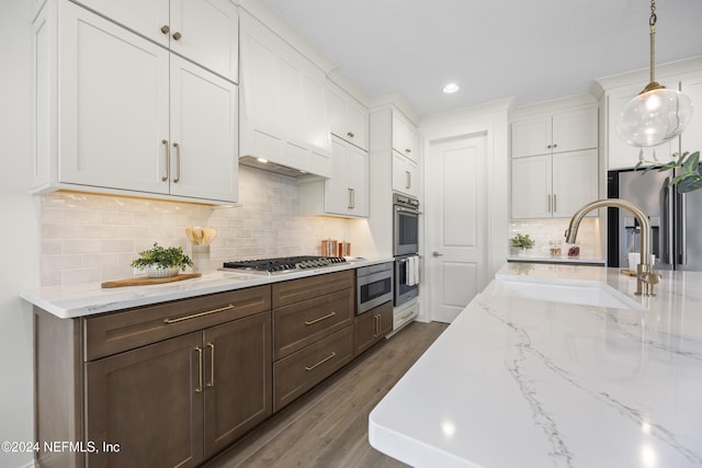 kitchen with hardwood / wood-style floors, sink, hanging light fixtures, white cabinetry, and stainless steel appliances