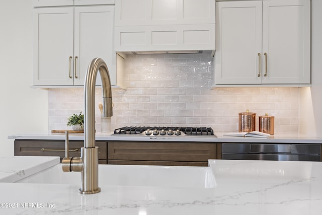 kitchen featuring stainless steel gas stovetop, decorative backsplash, white cabinetry, and light stone countertops