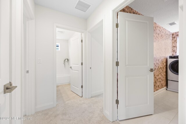 corridor featuring washer / dryer, a textured ceiling, and light colored carpet