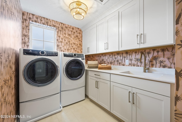 laundry room featuring washing machine and clothes dryer, an inviting chandelier, cabinets, and sink