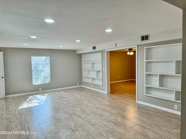 unfurnished room featuring built in shelves, a textured ceiling, and light hardwood / wood-style flooring