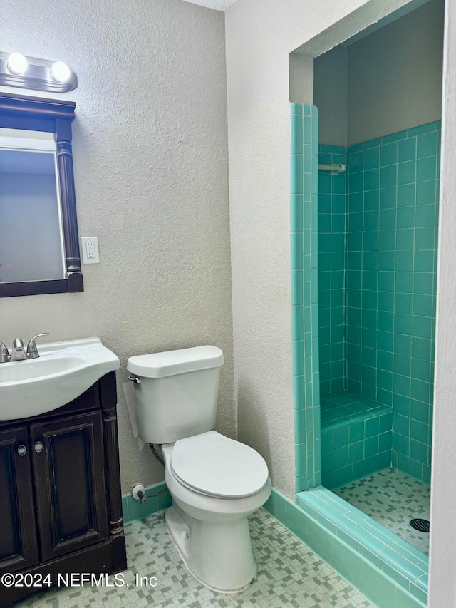 bathroom with tile patterned flooring, vanity, toilet, and tiled shower