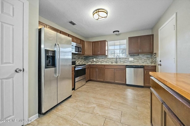 kitchen with decorative backsplash, sink, a textured ceiling, and appliances with stainless steel finishes