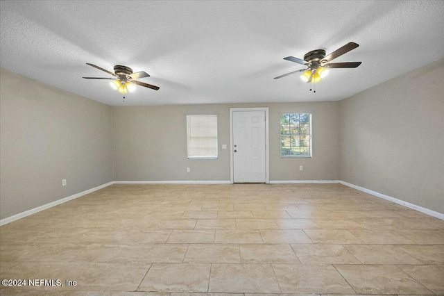 empty room with ceiling fan, light tile patterned flooring, and a textured ceiling