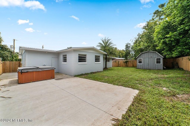 back of house featuring a shed, a yard, a patio, and a hot tub