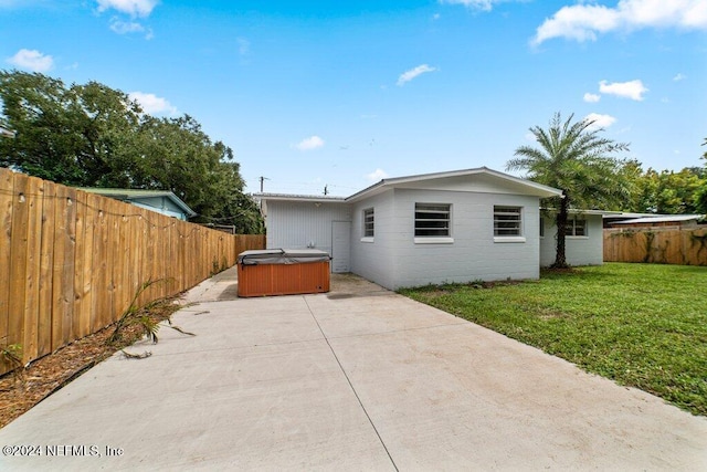 back of house featuring a yard, a patio, and a hot tub