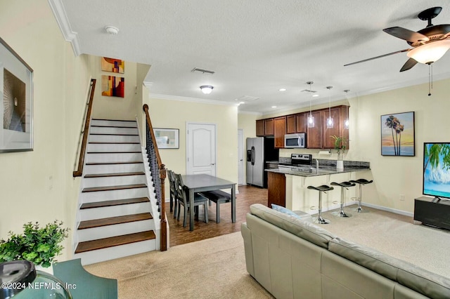 living room with a textured ceiling, light hardwood / wood-style flooring, ceiling fan, and crown molding