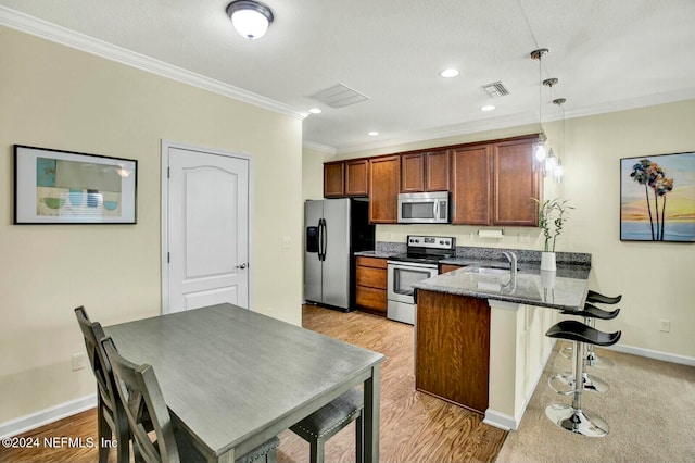 kitchen with pendant lighting, crown molding, light wood-type flooring, appliances with stainless steel finishes, and kitchen peninsula