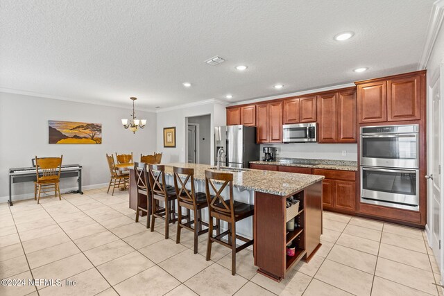 kitchen featuring stainless steel appliances, light stone counters, crown molding, decorative light fixtures, and a center island with sink