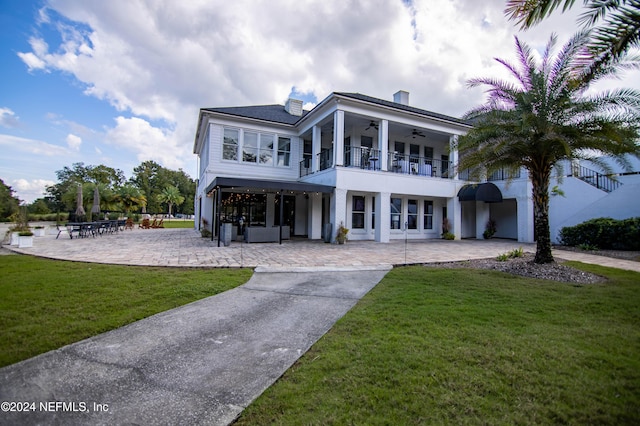 view of front of property featuring a front yard, ceiling fan, a balcony, and a patio