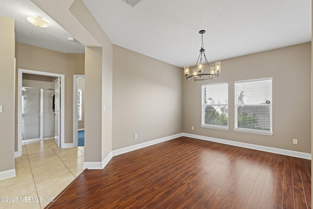 unfurnished room featuring light wood-type flooring, a notable chandelier, and a textured ceiling