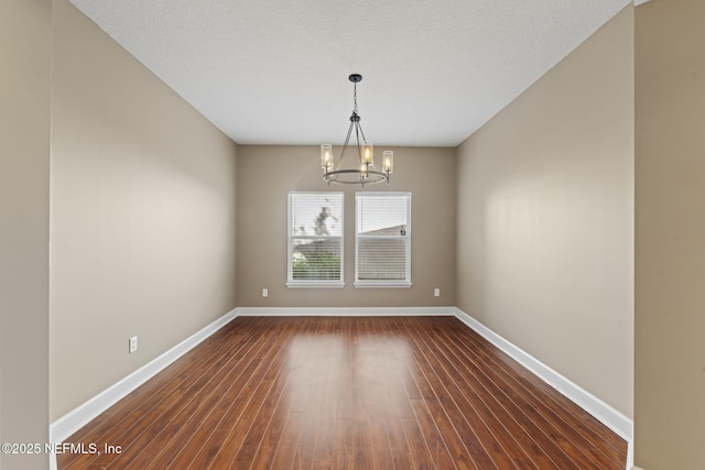 spare room featuring a textured ceiling, dark hardwood / wood-style floors, and a notable chandelier