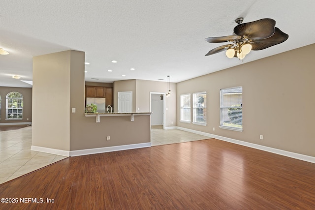 unfurnished living room featuring ceiling fan, a textured ceiling, and light hardwood / wood-style floors