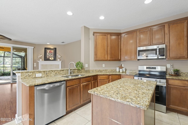 kitchen featuring kitchen peninsula, stainless steel appliances, sink, light stone countertops, and a center island