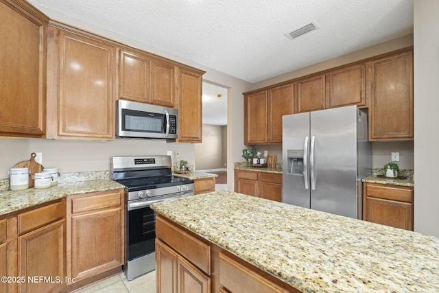 kitchen featuring light tile patterned flooring, appliances with stainless steel finishes, a textured ceiling, and light stone counters