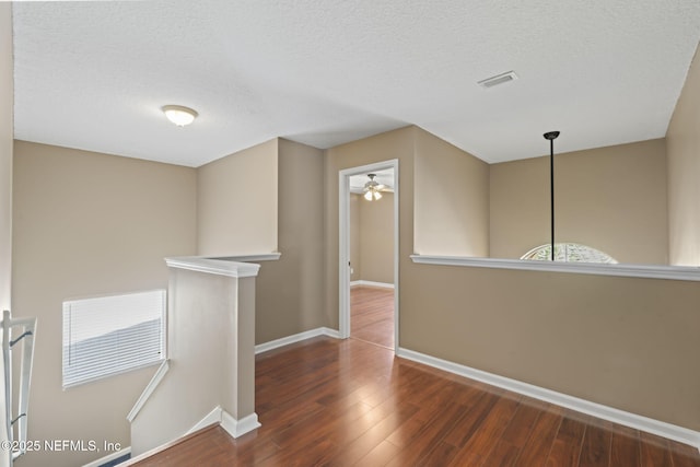 corridor with a textured ceiling and dark hardwood / wood-style flooring