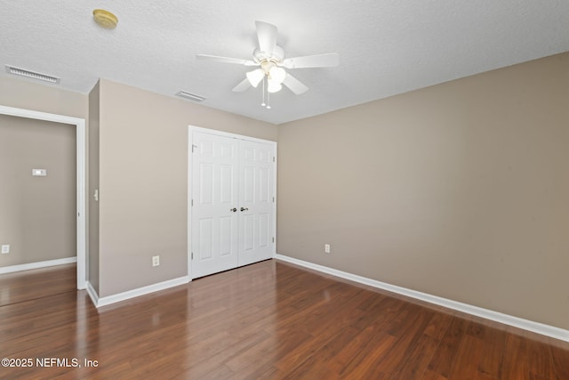 unfurnished bedroom featuring dark wood-type flooring, ceiling fan, a closet, and a textured ceiling