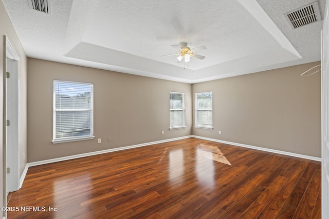 unfurnished room with a textured ceiling, dark wood-type flooring, a raised ceiling, and ceiling fan