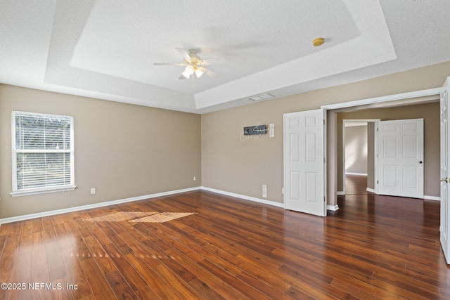 unfurnished room with a raised ceiling, ceiling fan, dark hardwood / wood-style flooring, and a textured ceiling