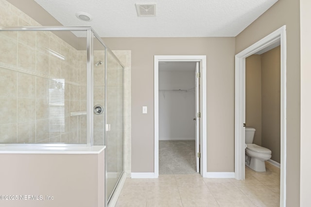 bathroom with tile patterned floors, toilet, a shower with door, and a textured ceiling