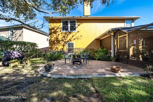 rear view of property with an outdoor fire pit, a sunroom, a yard, and a patio