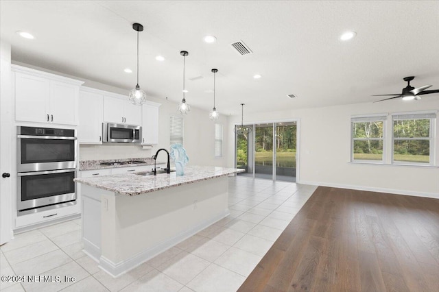 kitchen featuring stainless steel appliances, a kitchen island with sink, sink, pendant lighting, and white cabinetry