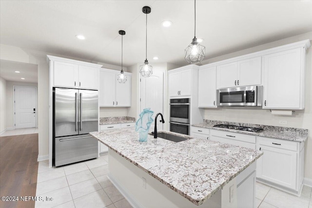 kitchen with appliances with stainless steel finishes, sink, decorative light fixtures, white cabinets, and an island with sink