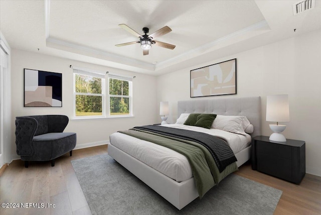 bedroom with wood-type flooring, a tray ceiling, ceiling fan, and crown molding