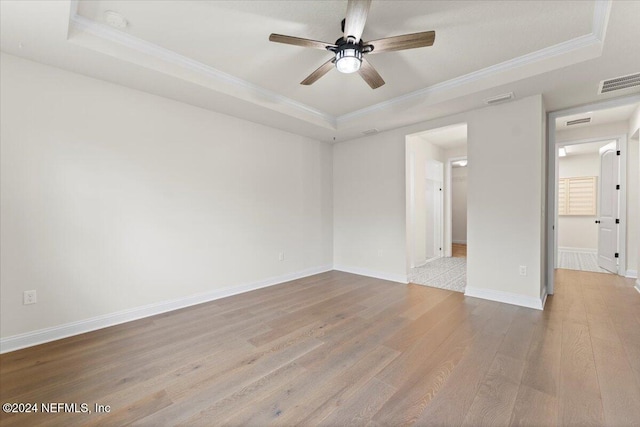 empty room with a raised ceiling, crown molding, light hardwood / wood-style flooring, and ceiling fan