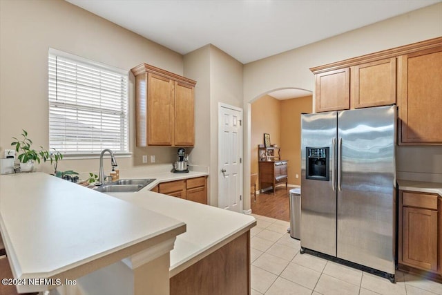 kitchen with kitchen peninsula, sink, light tile patterned floors, and stainless steel refrigerator with ice dispenser