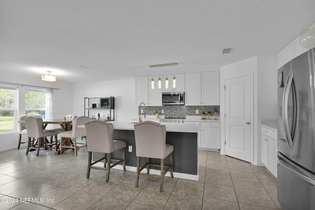 kitchen featuring pendant lighting, a kitchen island with sink, white cabinets, light tile patterned floors, and appliances with stainless steel finishes