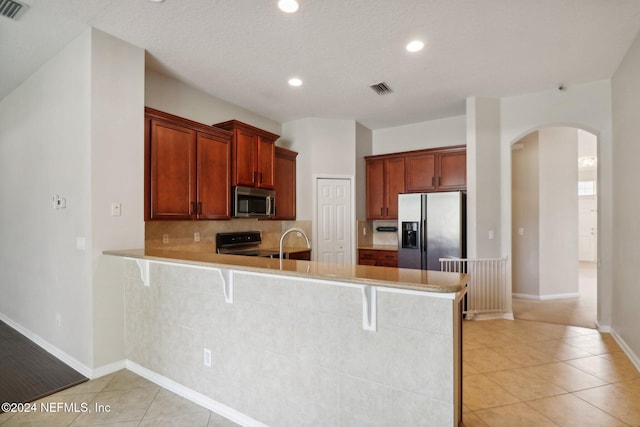 kitchen with kitchen peninsula, tasteful backsplash, a breakfast bar, stainless steel appliances, and light tile patterned floors