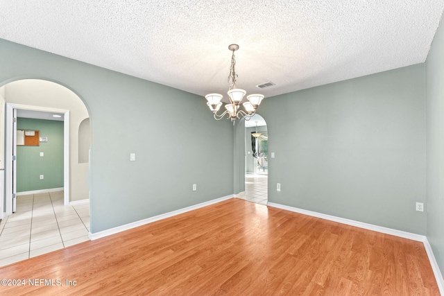 unfurnished room featuring a notable chandelier, light hardwood / wood-style floors, and a textured ceiling