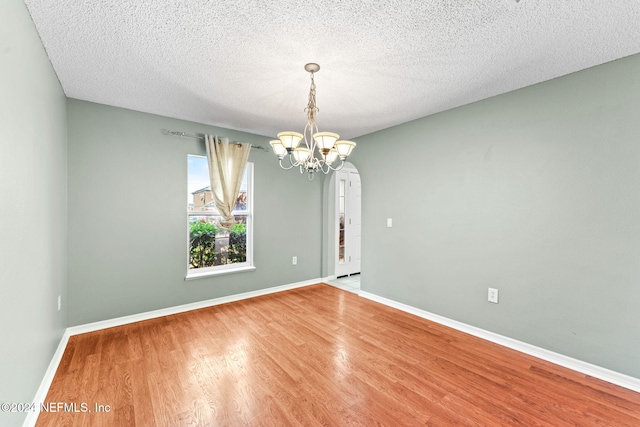 empty room featuring wood-type flooring, a textured ceiling, and a notable chandelier