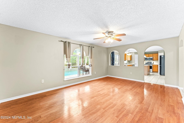 unfurnished living room with ceiling fan, light wood-type flooring, and a textured ceiling