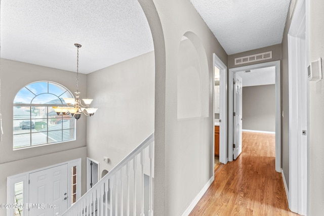 hallway featuring light hardwood / wood-style floors, a textured ceiling, and an inviting chandelier