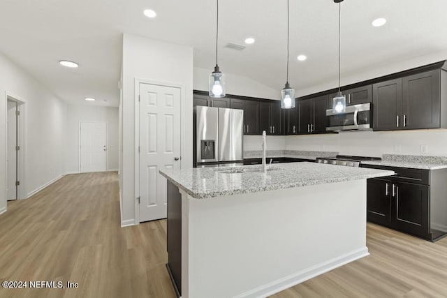 kitchen featuring appliances with stainless steel finishes, light wood-type flooring, light stone counters, a kitchen island with sink, and decorative light fixtures