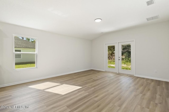 spare room with lofted ceiling, light wood-type flooring, and french doors