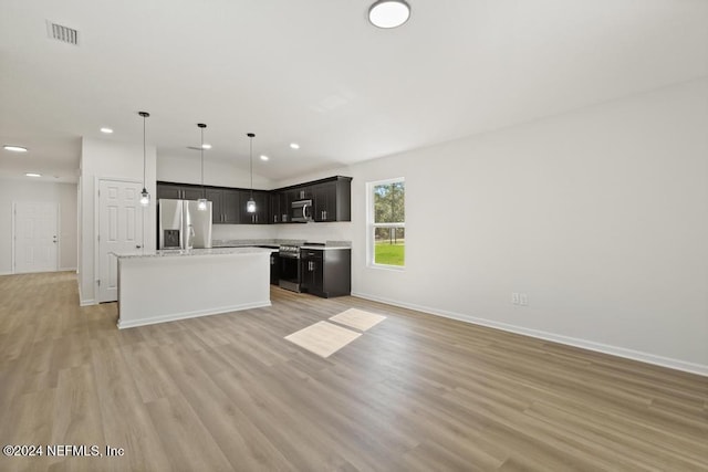 kitchen with appliances with stainless steel finishes, light wood-type flooring, light stone counters, a center island with sink, and hanging light fixtures