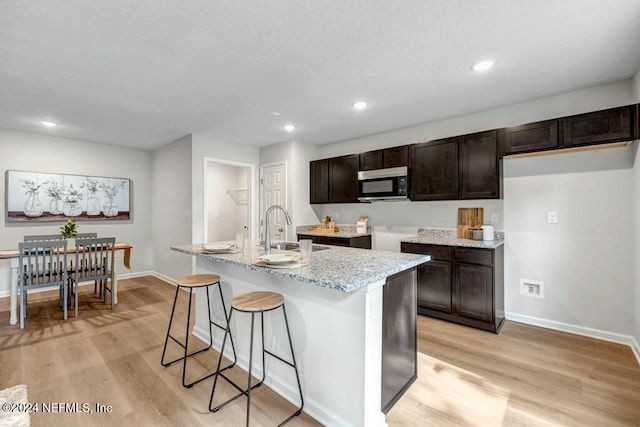 kitchen with light stone counters, sink, a kitchen island with sink, and light hardwood / wood-style flooring