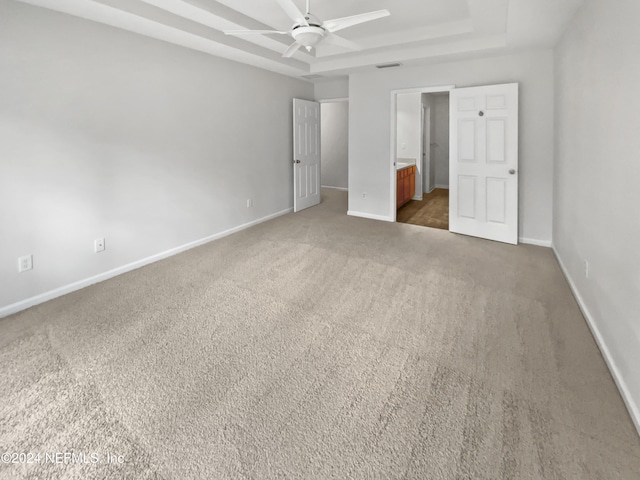 unfurnished bedroom featuring connected bathroom, carpet floors, ceiling fan, and a tray ceiling