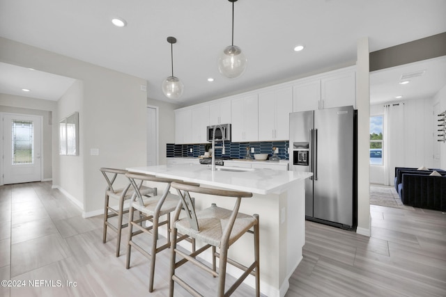 kitchen with a center island with sink, appliances with stainless steel finishes, white cabinetry, and pendant lighting