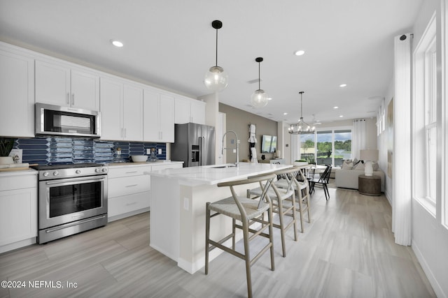 kitchen with stainless steel appliances, a kitchen breakfast bar, decorative light fixtures, a kitchen island with sink, and white cabinets