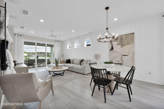 dining area featuring ceiling fan with notable chandelier and wooden walls