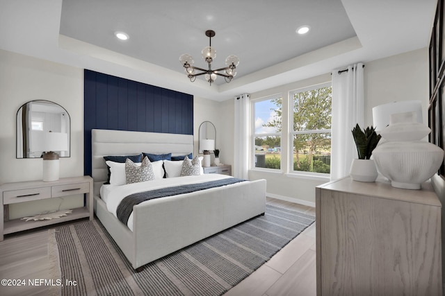 bedroom with a tray ceiling, light hardwood / wood-style floors, and a notable chandelier