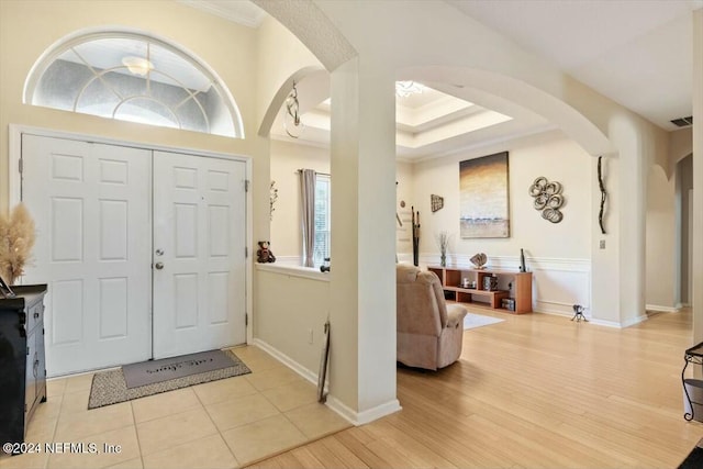 foyer entrance with a tray ceiling, light wood-type flooring, and ornamental molding