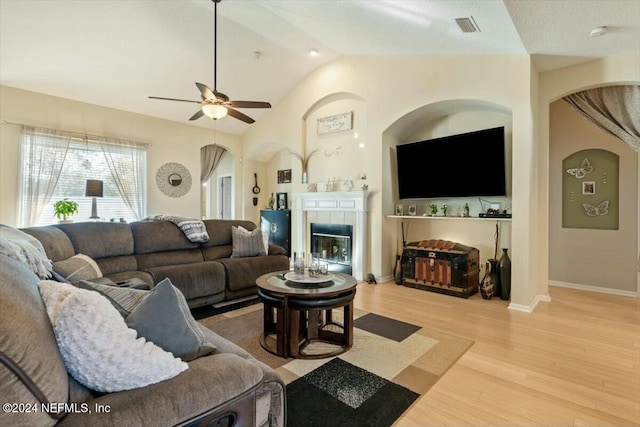 living room featuring hardwood / wood-style floors, ceiling fan, lofted ceiling, and a tiled fireplace