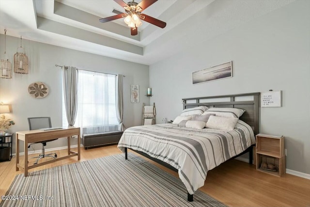 bedroom with a raised ceiling, ceiling fan, and light hardwood / wood-style flooring