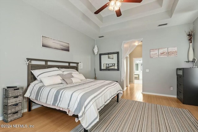 bedroom with hardwood / wood-style flooring, ceiling fan, and a tray ceiling