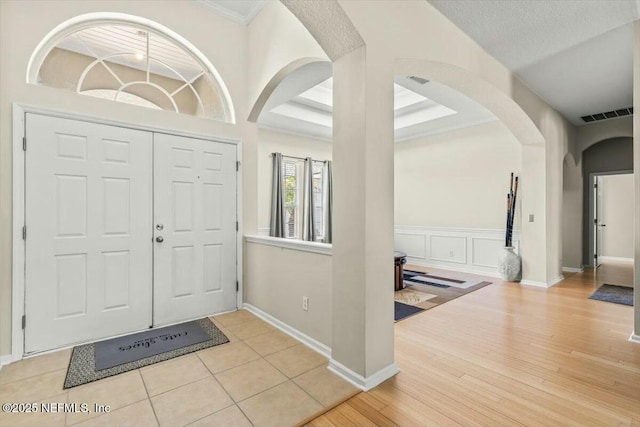 foyer entrance with ornamental molding, arched walkways, visible vents, a decorative wall, and wood finished floors